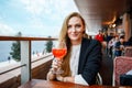 Young business woman drinking alcoholic cocktail. Happy alone woman in outdoor cafe or restaurant on sunny summer day, break for Royalty Free Stock Photo