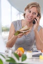 Young business woman eating salad at a large windows office, having healthy lunch at workplace while using phone and