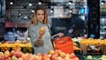 Young business woman girl buyer client blonde lady consumer stands in shop near counter with fruits in grocery store