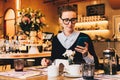 Young business woman in glasses sits in cafe at table, uses smartphone. On table is cup of coffee. Girl working Royalty Free Stock Photo