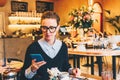 Young business woman in glasses sits in cafe at table, uses smartphone. On table is cup of coffee. Girl working Royalty Free Stock Photo