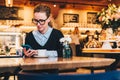 Young business woman in glasses sits in cafe at table, uses smartphone. On table is cup of coffee. Girl working Royalty Free Stock Photo