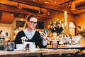 Young business woman in glasses sits in cafe at table, uses smartphone. On table is cup of coffee. Girl working Royalty Free Stock Photo