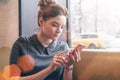 Young business woman in gray dress sitting near window and uses your smartphone.In background is blurred yellow taxi.