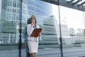 The young business woman in gray office dress holds in hand folder with documents. Businesswoman standing next to the business cen Royalty Free Stock Photo