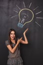 A young business woman has a great idea and raises her hands up pointing to a lightbulb on the board. Royalty Free Stock Photo