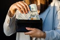 Young business woman hides US dollars in a black wallet, close up of female hands. The concept of cash payments, savings