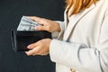 Young business woman hides US dollars in a black wallet, close up of female hands. The concept of cash payments, savings