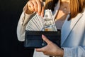 Young business woman hides US dollars in a black wallet, close up of female hands. The concept of cash payments, savings