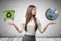 Young business woman holding earth globe and green trash can in her hands on grey wall background Royalty Free Stock Photo