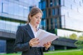 Young business woman holding papers in business clothes on city street against Royalty Free Stock Photo