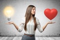 Young business woman holding red heart and yellow light bulb in her hands on grey wall background Royalty Free Stock Photo