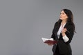 Young business woman with notepad and pen close to her chin. Pensive business lady writing on clipboard standing over Royalty Free Stock Photo