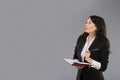 Young business woman with notepad and pen close to her chin. Pensive business lady writing on clipboard standing over Royalty Free Stock Photo