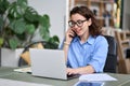 Young business woman working online on laptop making call on cell phone.