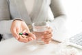 Young business woman sick in the office, hand holding pills and water glass. pills, tissue and laptop on table. Royalty Free Stock Photo