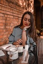 Young business woman sitting in cafe drinking coffee. Beautiful girl is working against an orange brick wall. View of freelancer Royalty Free Stock Photo