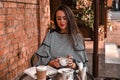 Young business woman sitting in cafe drinking coffee. Beautiful girl is working against an orange brick wall. View of freelancer Royalty Free Stock Photo