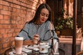 Young business woman sitting in cafe drinking coffee. Beautiful girl is working against an orange brick wall. View of freelancer Royalty Free Stock Photo