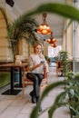 Young business woman sitting in cafe at table, leaning his hand back in chair, looking out window and holding smartphone Royalty Free Stock Photo