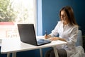 Young business woman sitting in cafe writing notes in notebook, freelancer working online using laptop, looking for job Royalty Free Stock Photo