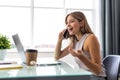 Young business woman sitting at office desk and talking on cell phone Royalty Free Stock Photo