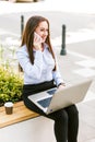 Young business woman sitting outdoor talking on phone while working on laptop Royalty Free Stock Photo