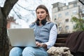 Young business woman sitting in park on bench working on laptop computer listening music on wireless headset. Businessperson Royalty Free Stock Photo