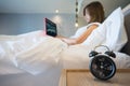 Young business woman sitting in white bed working on the laptop computer with alarm clock on foreground Royalty Free Stock Photo