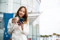 Asian businesswoman with smartphone and cup coffee standing against street building near office Royalty Free Stock Photo