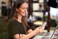 Young business woman smiling, sitting at desk in the office, working from home, using laptop computer and mobile phone, checking Royalty Free Stock Photo