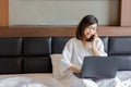 Young business woman talking on phone and using moble phone on bed while working from home during covid -19 crisis