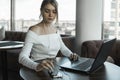 Young business woman using laptop computer in cafe or in coworking and texting a message on a smart phone. Blond female Royalty Free Stock Photo