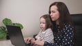 Young business woman works in a home office with a laptop with a child in her arms, a freelancer at a computer at remote Royalty Free Stock Photo