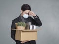 Young businessman being fired, holding a cardboard box with office supplies, standing in front of gray wall