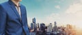Young businessman in blue suit, blurred modern city in sunrise background