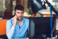 Young businessman busy working on laptop computer while talking on the smart-phone at office. Royalty Free Stock Photo