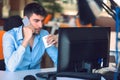 Young businessman busy working on laptop computer while talking on the smart-phone at office. Royalty Free Stock Photo