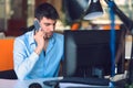 Young businessman busy working on laptop computer while talking on the smart-phone at office. Royalty Free Stock Photo