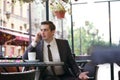 A young businessman came to lunch in a cafe, he sits at a table and talking by smartphone with bad emotions