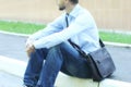 Young businessman in casual clothes with leather brief bag sitting on the pavement near office building. Urban city lifestyle Royalty Free Stock Photo