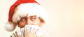 Young businessman in Christmas Hat covered his face with money over white background, copy space. Santa holding up fanned out hand Royalty Free Stock Photo