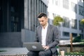 Young businessman in the city sits on bench, takes a laptop and works. Businessman typing on laptop computer outdoor Royalty Free Stock Photo