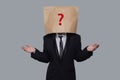 Young businessman covering his face using a craft paper bag with red drawn question mark, like a mask, for hiding his identity. Royalty Free Stock Photo