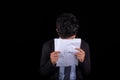 Young businessman crying over a document and covering his face, isolated on black background. Royalty Free Stock Photo