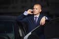 Young businessman in dark blue suit calling on cell phone leaning on his car Royalty Free Stock Photo