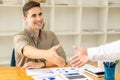 A young businessman does if to shake his colleague`s hand as a welcome in teamwork with a financial graph on the table.