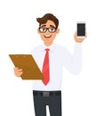 Young businessman in eye glasses holding clipboard and showing mobile, cellphone or smartphone screen. Person carrying document. Royalty Free Stock Photo