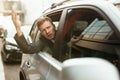 Young businessman feels nervous looking out from the open car window stuck in traffic jam, big city life