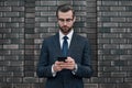 A young businessman in glasses and an expensive suit, works on a smarphone in his hands